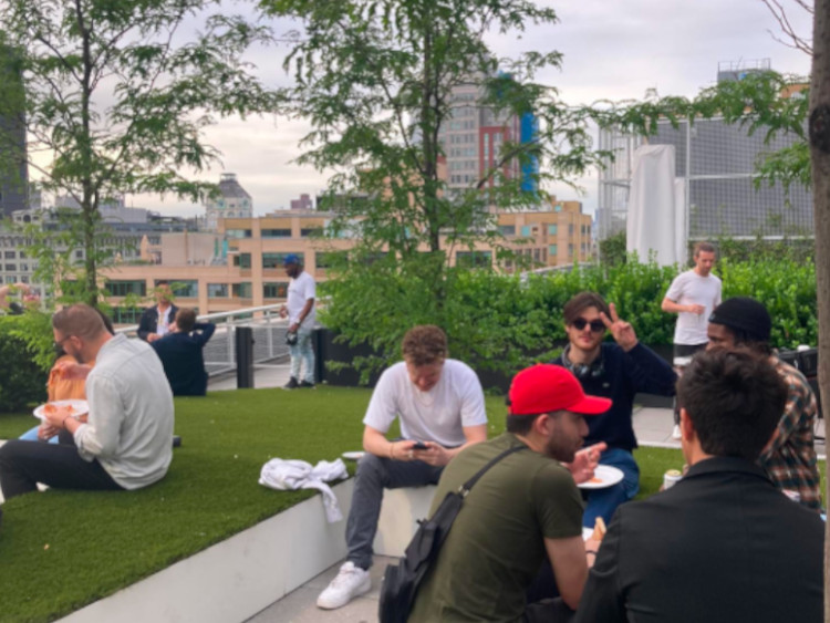 A picture of people sitting down in groups on a grassy rooftop. One person is giving a peace sign
